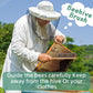 Beekeeper suit with mesh veil holding a hive frame and bee brush