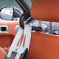 Black seat hook holding two seatbelt straps on rear headrest posts