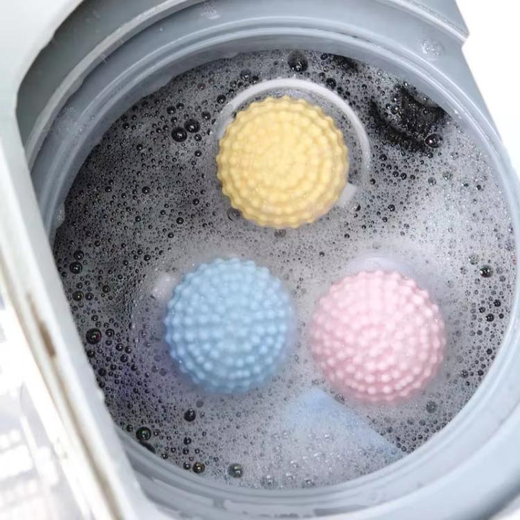 Washing machine drum with three hair lint catcher balls: yellow, blue, and pink