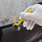 Yellow plastic film edge scraper held in white glove, for tucking window film