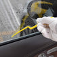 Yellow plastic scraper tool for smoothing and tucking car window film, held by glove