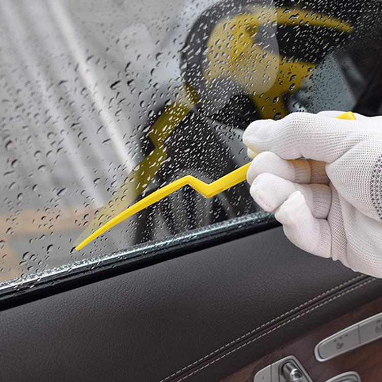 Yellow plastic scraper tool for smoothing and tucking car window film, held by glove