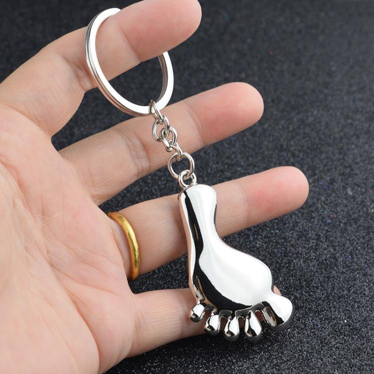 Silver metal foot-shaped keychain charm held in an open hand