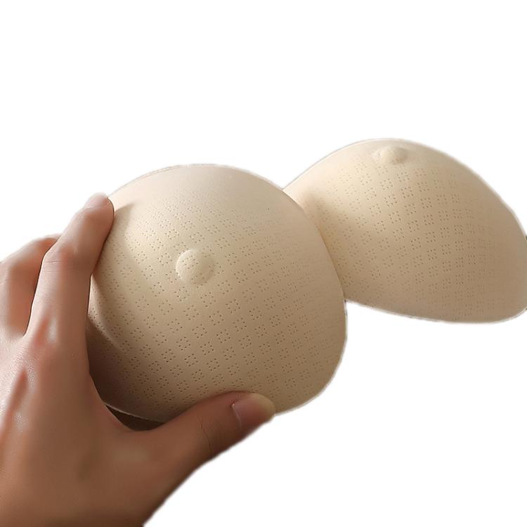 Two beige prosthetic breast pads with textured surface, held by hands