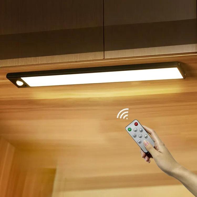 Silver motion-sensor light bar with remote control in hand under cabinet