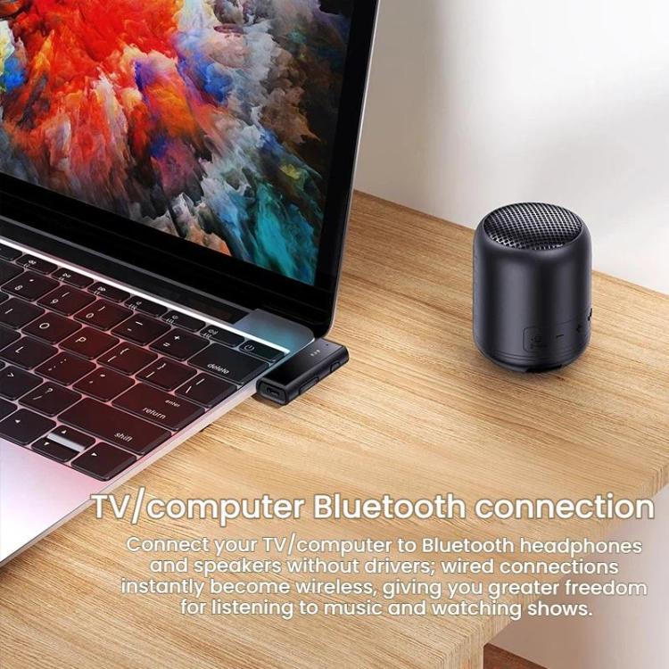 Black Bluetooth audio receiver puck on wooden desk beside laptop