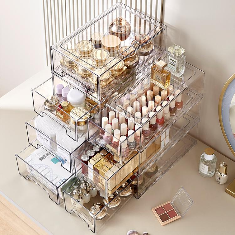 Stack of clear acrylic drawer organizers holding cosmetics, bottles, and small containers