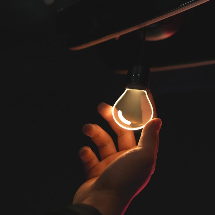 Hand holding a glowing car LED pendant light bulb with black cap and teardrop shape