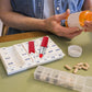 Red lipstick-shaped pillbox with cap off next to pills and blister cards.