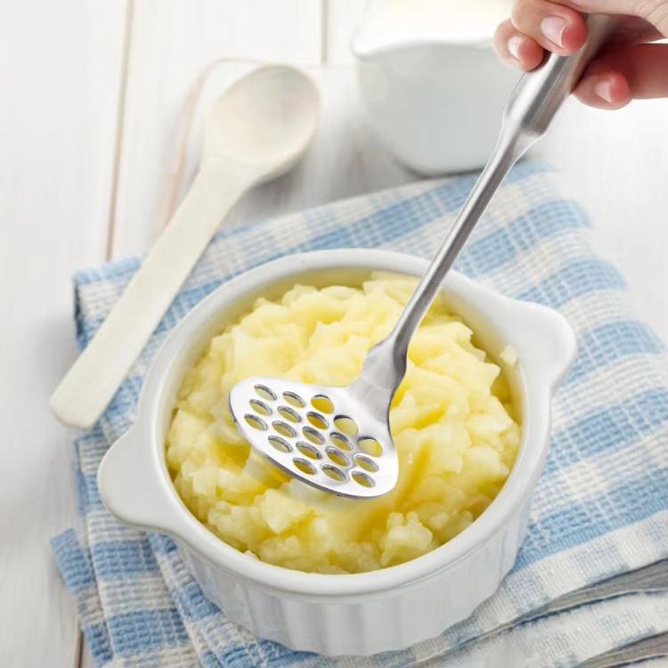Stainless steel potato masher mashing potatoes in a white bowl