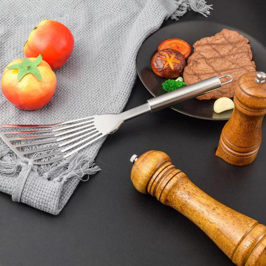 Stainless steel slotted spatula with angled fork head on a skillet