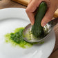 Perforated stainless steel grinder spoon grating a green vegetable onto a plate