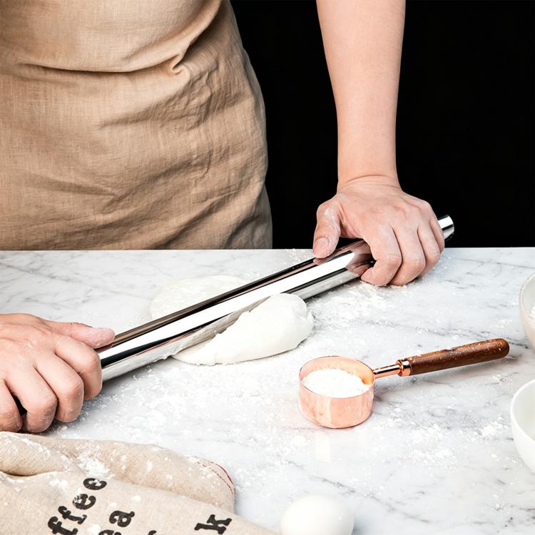 Stainless steel rolling pin with parallel rods, used to smooth dough on a countertop