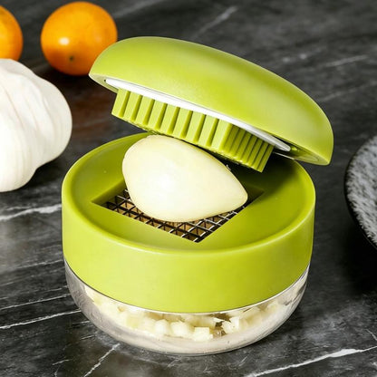 Green manual garlic press with clear bowl and hinged grater, garlic clove inside.