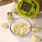 Green manual garlic press grating plate over a bowl of chopped garlic pieces.