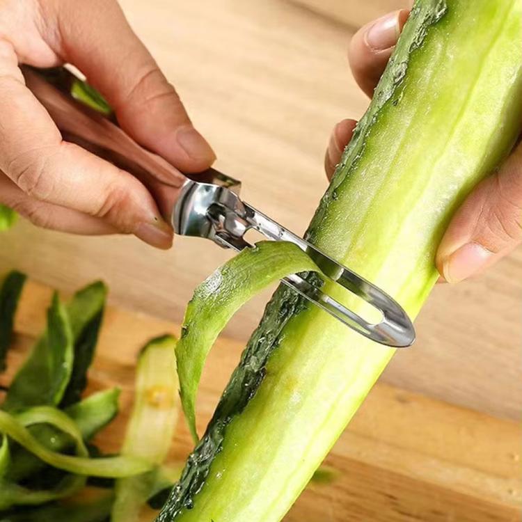 Fruit peeler removing long peels from a green vegetable held on a board.