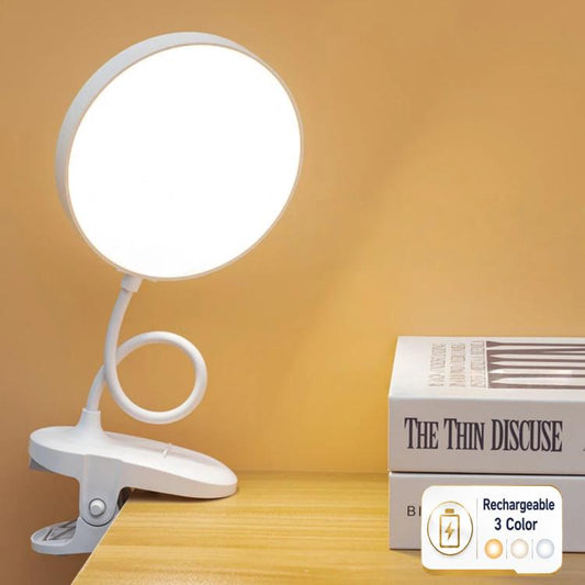 White round LED clip-on desk lamp on wooden desk with glowing circular head