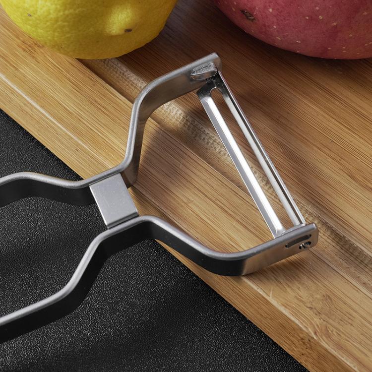 Stainless steel peeler blade assembly with curved frame, angled on cutting board