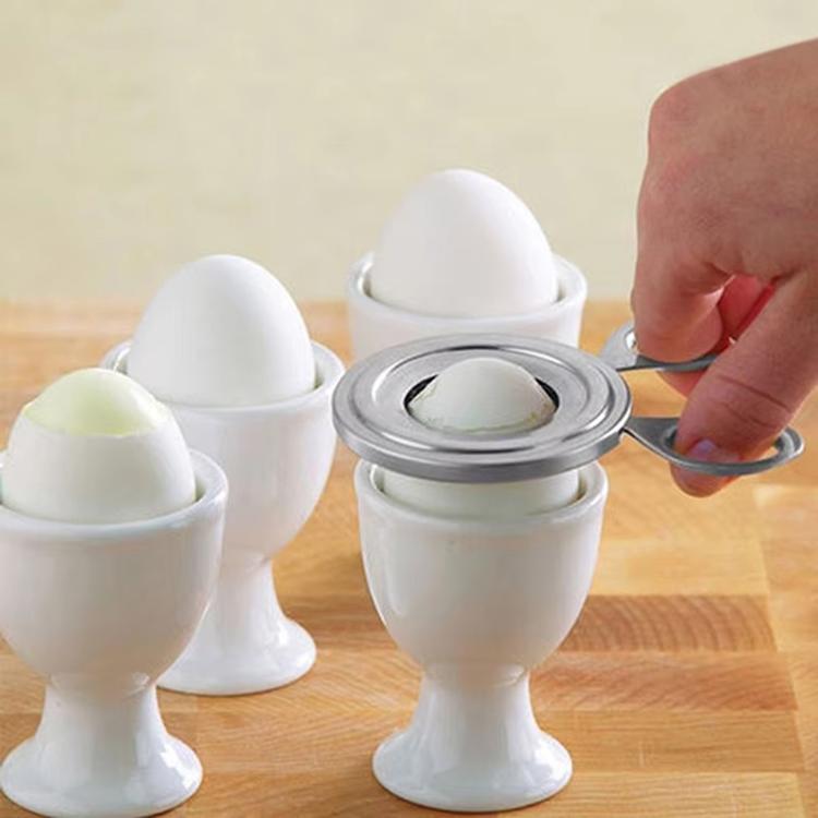 Stainless steel egg cracker tool on boiled eggs in white egg cups