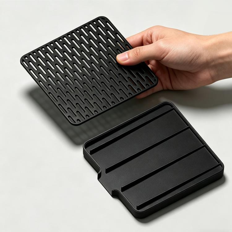 Black perforated espresso drip tray lifted by hand above a sloped base