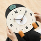 Small mantel table clock held by hands, cream dial with black hands and orange pegs