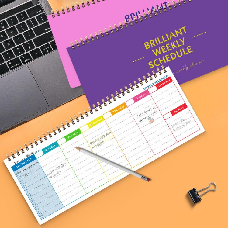 Two undated weekly planner pads, pink and purple covers, with gold spiral binding and pen