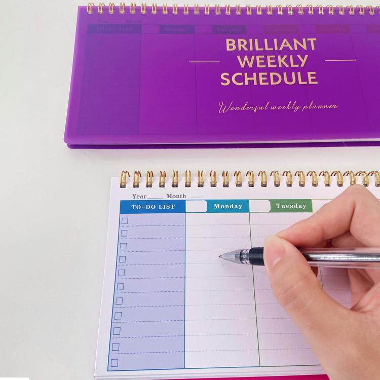 Purple undated weekly planner pad with gold spiral binding; hand writes in the schedule