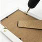 Gold D-ring picture hanger hook screwed to the frame edge on a board