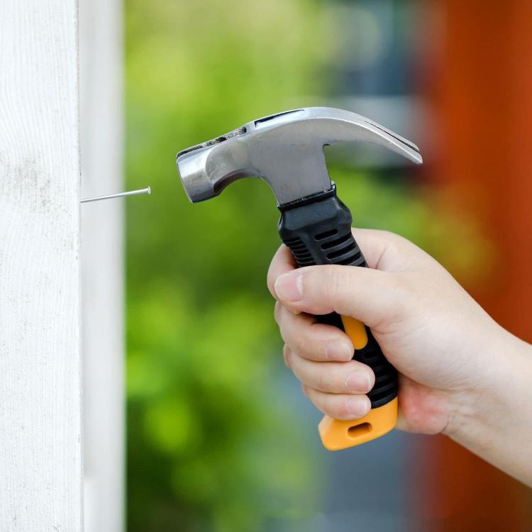 Hand holding a claw hammer inserting a nail into a wall for picture hanging