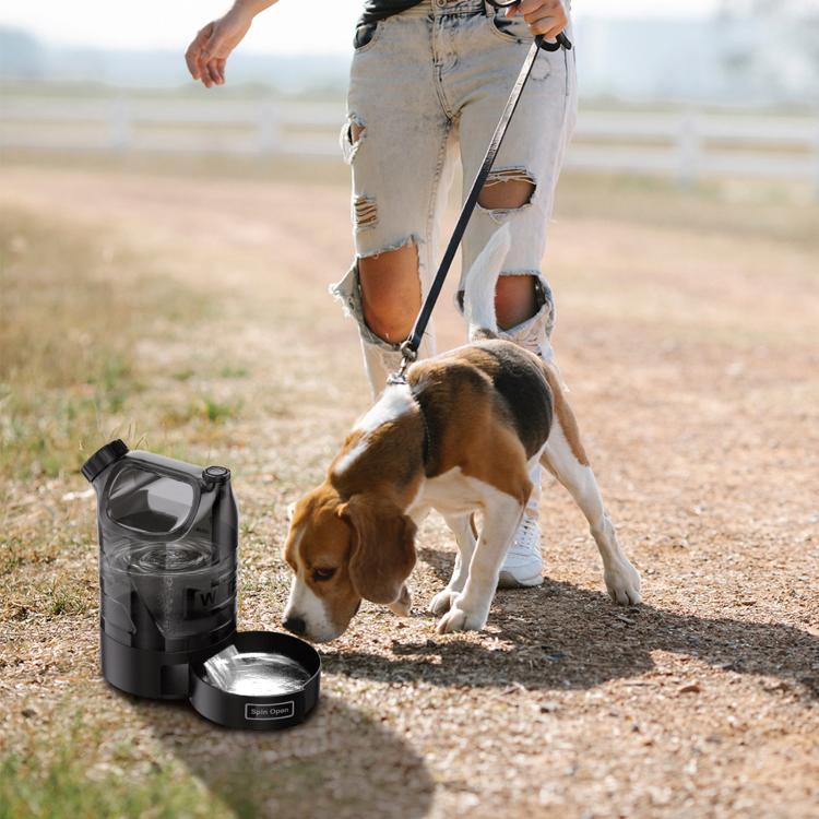Black outdoor water bottle with round drinking bowl base, near a walking dog