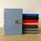 A5 6-hole magnetic buckle notebooks, stacked in blue, black, red, tan and green