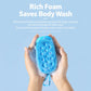 Hands holding a blue oval silicone scrubber over foam, with lanyard loop at the bottom.