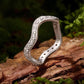 Curved wave moissanite ring in polished sterling silver resting on a rock surface