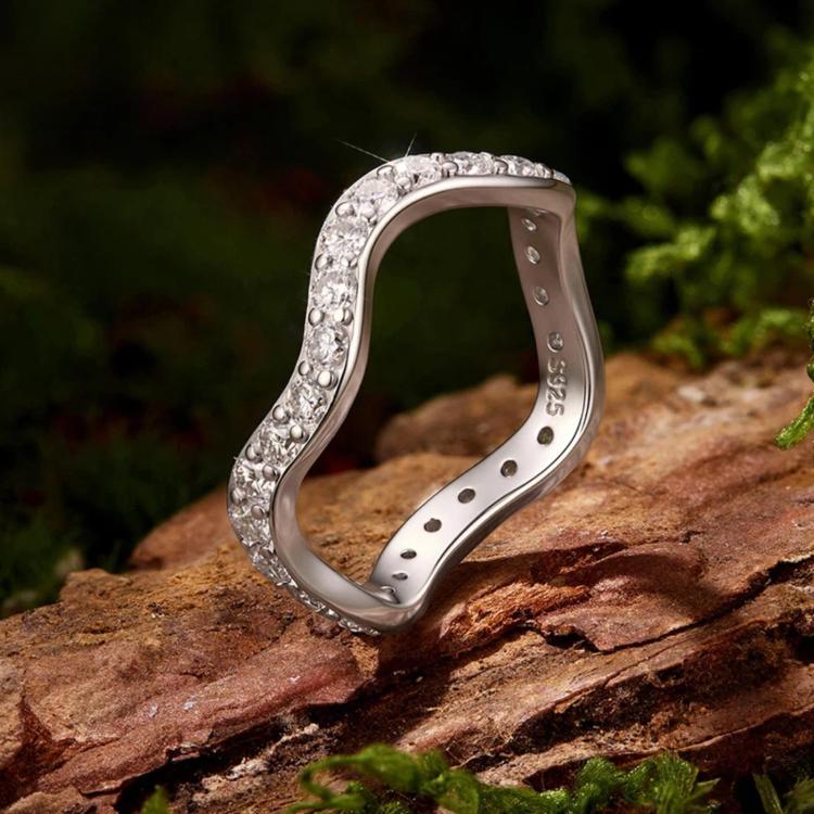 Curved wave moissanite ring in polished sterling silver resting on a rock surface