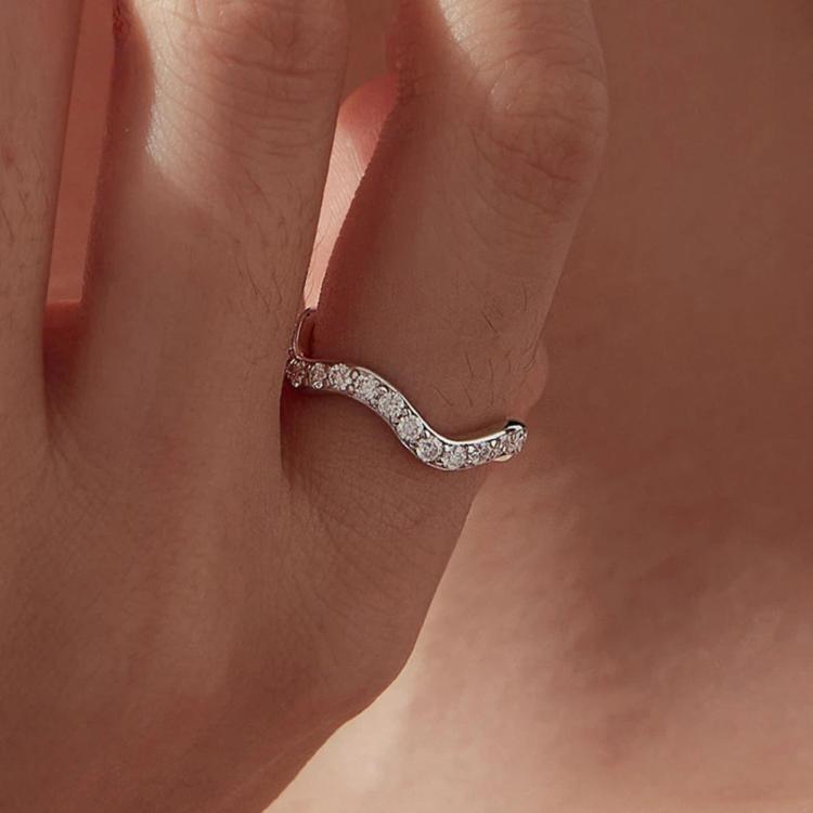 Slim wave moissanite ring on finger with sparkling stones along the curved band
