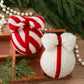 Two knitted bow ornaments—striped red-and-white and white—with hanging red cords