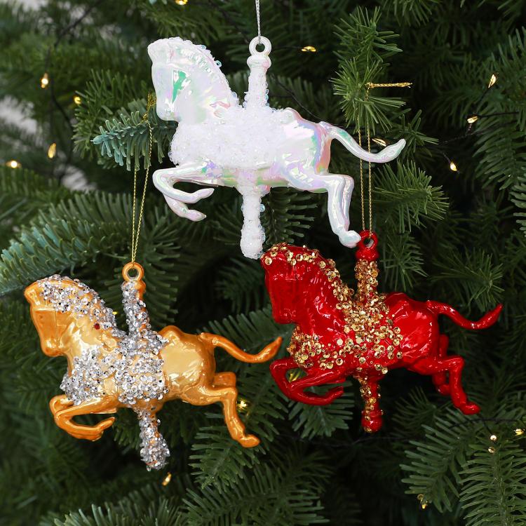 Three glitter rocking horse ornaments in white, gold, and red on a tree