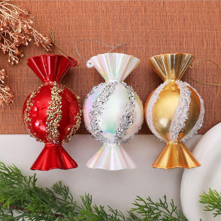 Three candy-shaped Christmas ornaments: red, iridescent white, and gold with glitter trim