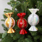 Candy-shaped Christmas ornaments in gold, red, and iridescent white hanging on a fir tree