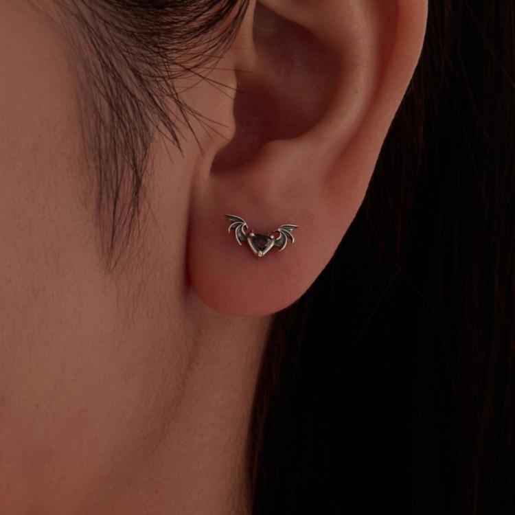 Sterling silver bat stud earrings worn on ear with purple heart-shaped gemstone