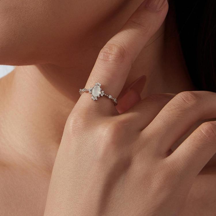 Moonstone ring on finger with oval pale center stone and small prong-set accents on band