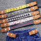 Stacked kids elastic belts with tan snap tabs on printed stripes and plaid fabric straps.