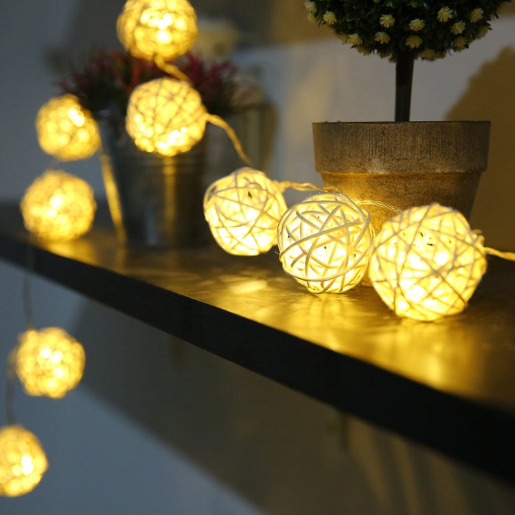 Warm white LED rattan ball string lights with woven globe bulbs on a shelf.