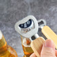 Stainless bottle opener with rubber wood handle prying a beer bottle cap