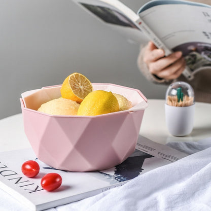 Pink double-layer drain basket with perforated base, holding lemons