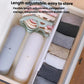 White plastic drawer divider with adjustable panels, separating folded blankets and garments.