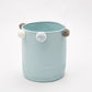 Light blue round storage basket with fluffy pom-pom accents on the side handles