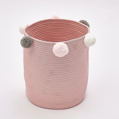 Pink fabric storage basket with fluffy pom-pom accents and round top opening