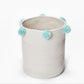Cream fabric storage basket with light blue pom-pom handles and round rim