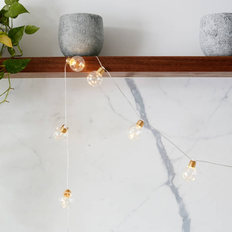 Copper wire LED string lights with warm clear globe bulbs and gold caps, close-up